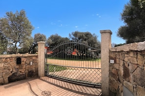A gated entrance with a stone wall, a metal gate, and a number sign indicating the location. - Domos Pintadas Cottage Rosa (Olbia)