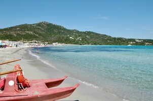 Una playa con agua turquesa cristalina, una orilla arenosa y una fila de barcos rojos.