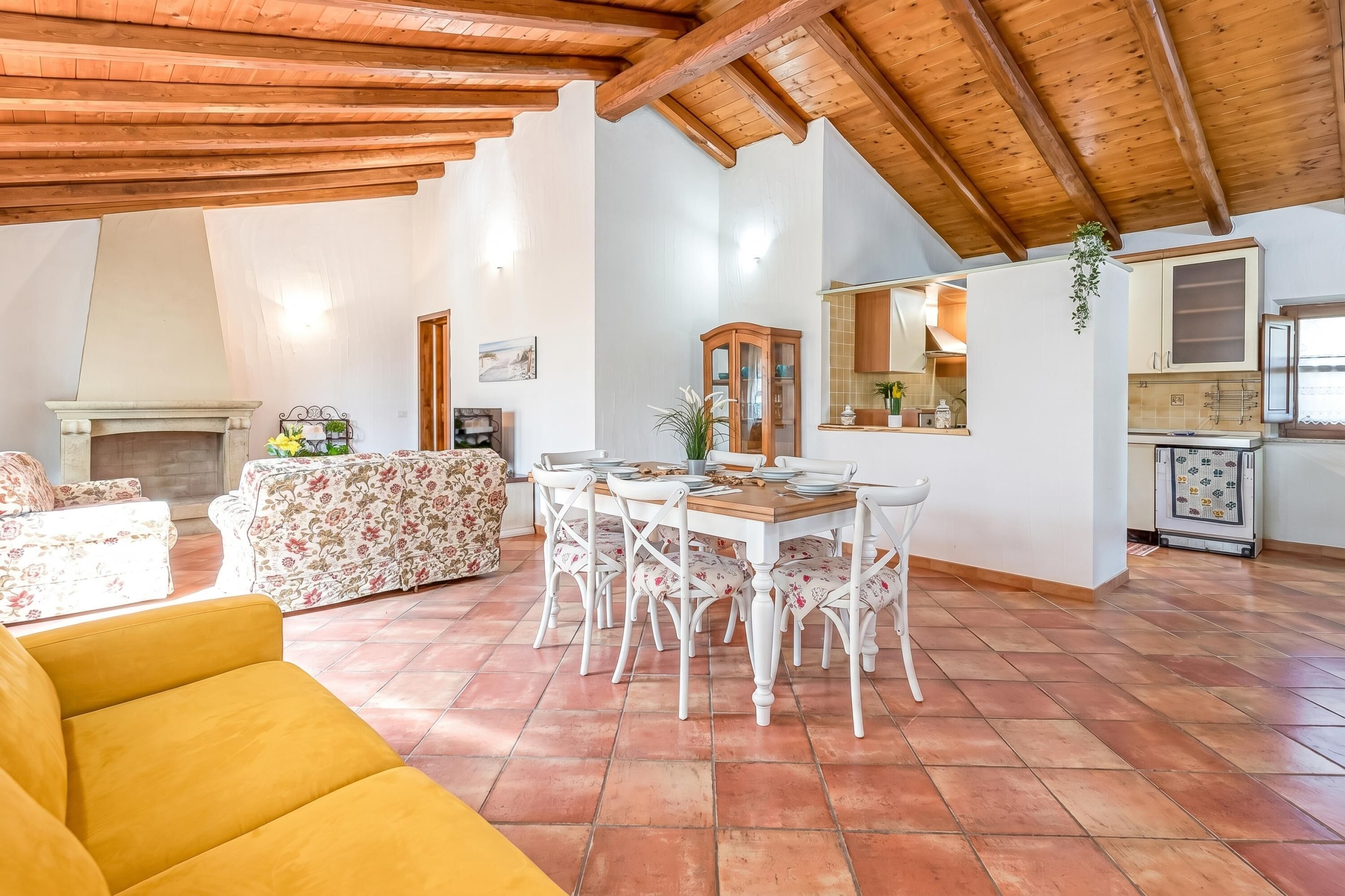 Un'ampia zona giorno con tavolo da pranzo, sedie, divano e cucina sullo sfondo.