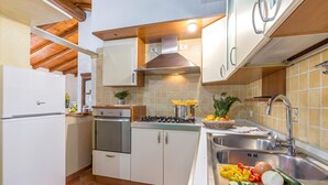 A kitchen with white cabinets, a stove, a sink, and various fruits and vegetables on the counter. - Domos Pintadas Cottage Rosa (Olbia)