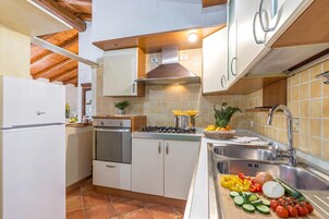 Una cocina con armarios blancos, una estufa, un fregadero y una variedad de frutas y verduras sobre la encimera.