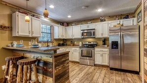 A kitchen with white cabinets, stainless steel appliances, a wooden island with stools, and decorative items on the ceiling. - Stoneybrook Valley Ranch 2,  3Bed/2Bath, DOG Friendly, 1.5 Acres Great Mtn views (Sevierville)