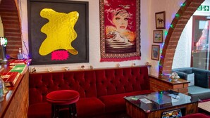 Uma área de bar com um banco estofado vermelho, um balcão de madeira e uma obra de arte emoldurada na parede.