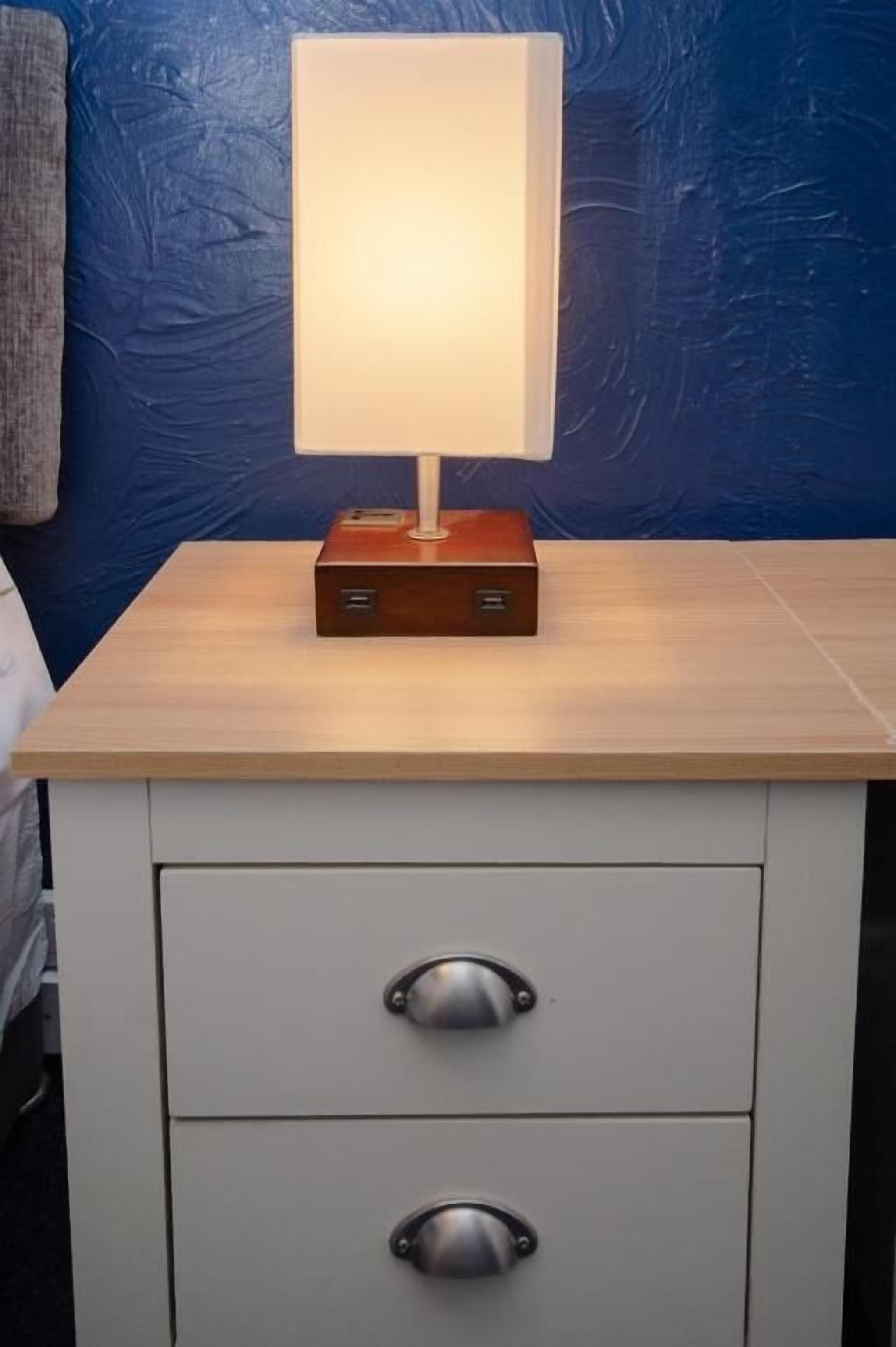 A bedside table with a lamp, two drawers, and a blue textured wall in the background.