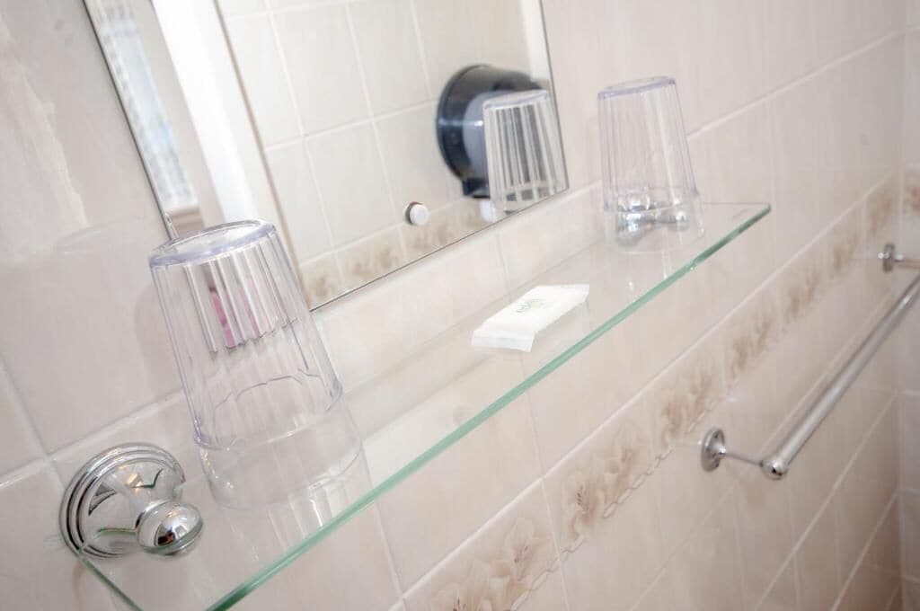 A bathroom with a glass shelf holding toiletries, a towel rack, and a mirror.