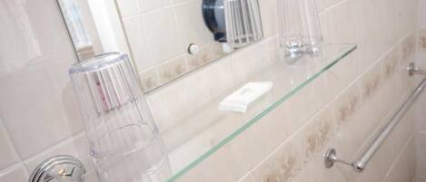 A bathroom with a glass shelf holding toiletries, a towel rack, and a mirror.