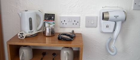 A wooden shelf with a kettle, a coffee maker, a phone, and a bag of tissues.