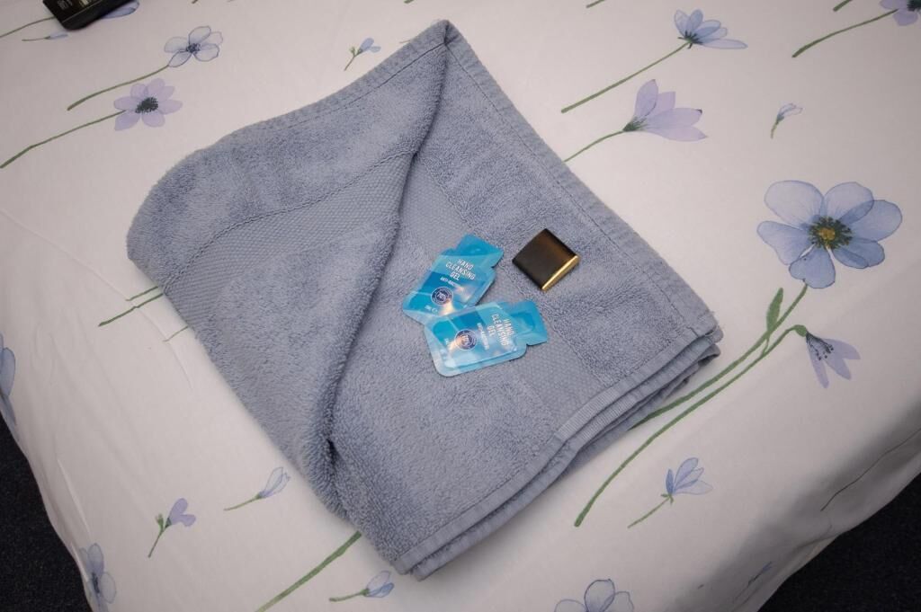 A folded towel and two blue packets on a bed with a floral pattern.