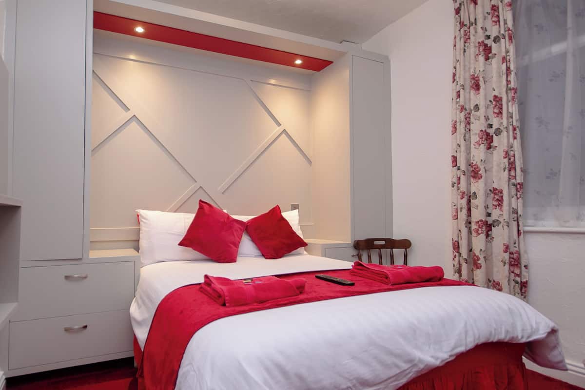 A neatly made bed with red bedding and pillows, a wooden chair, and a red accent wall.