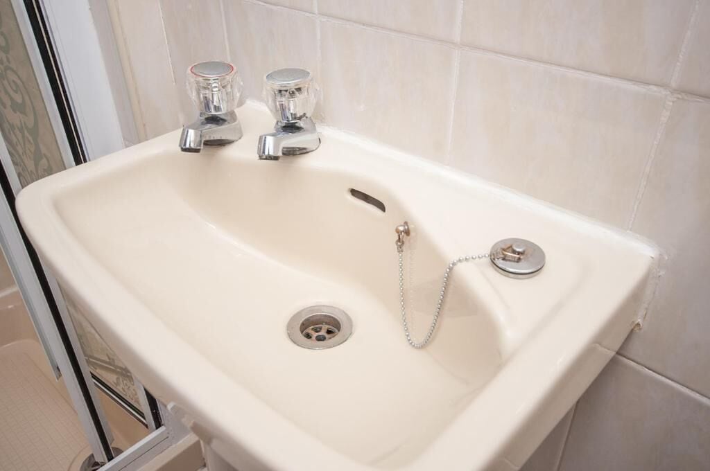 Un lavabo blanc pour la salle de bain, doté de deux robinets et d’un drain.