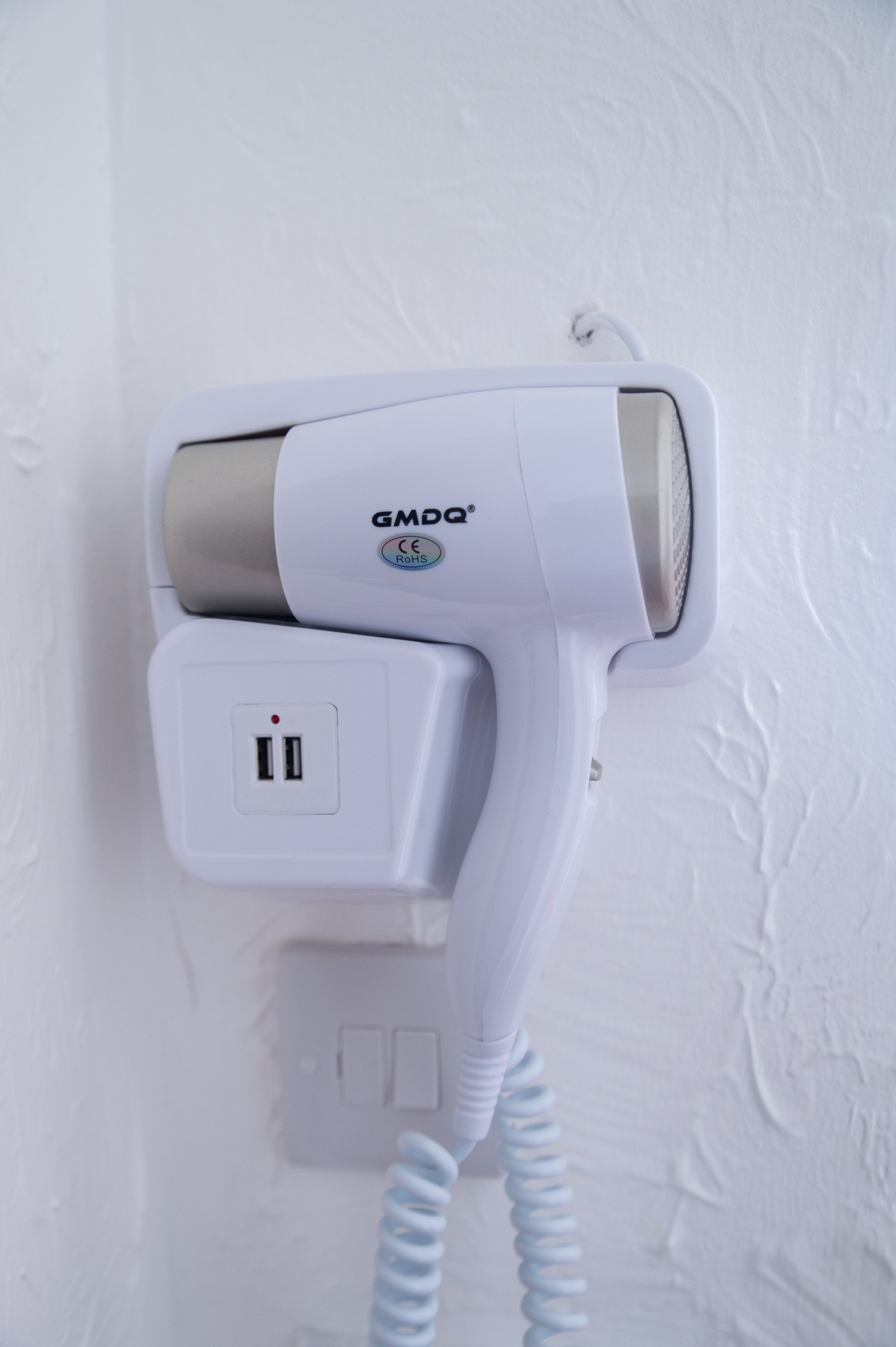 A wall-mounted hair dryer with a power cord, a plug, and a GMDQ logo.