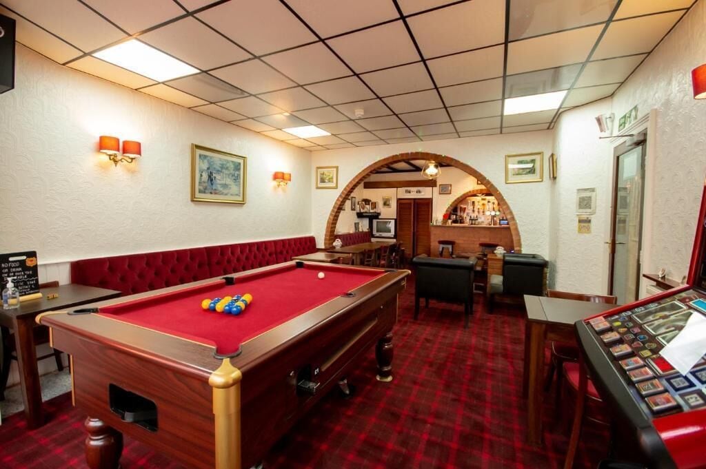 A billiards room with a pool table, seating area, and a bar.