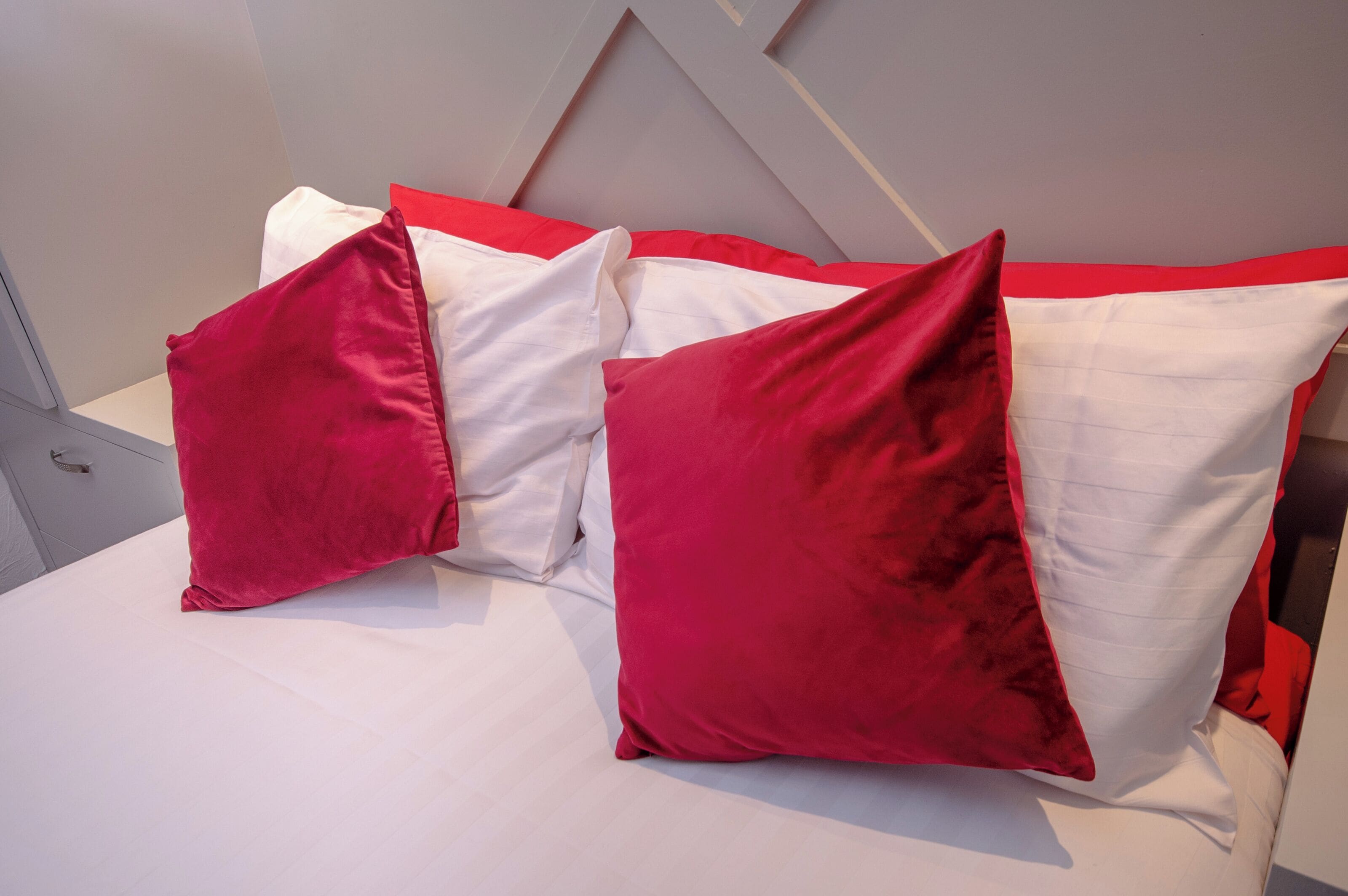 A bed with white and red bedding, including pillows and a red accent pillow.