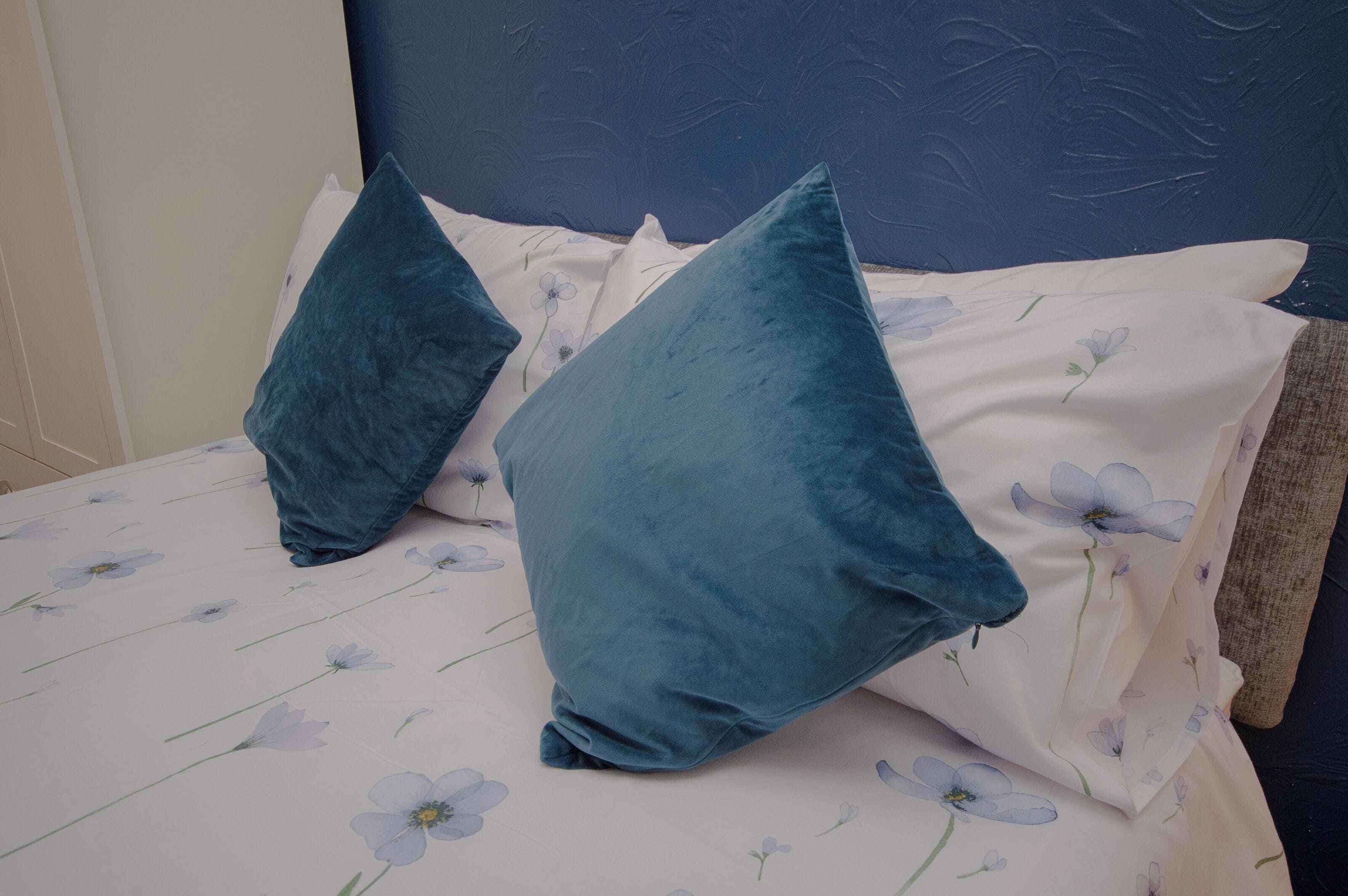 A bed with a floral bedspread and two teal pillows.