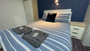 Quarto de hotel com cama, guarda-roupa, mesa de cabeceira e luz na parede.