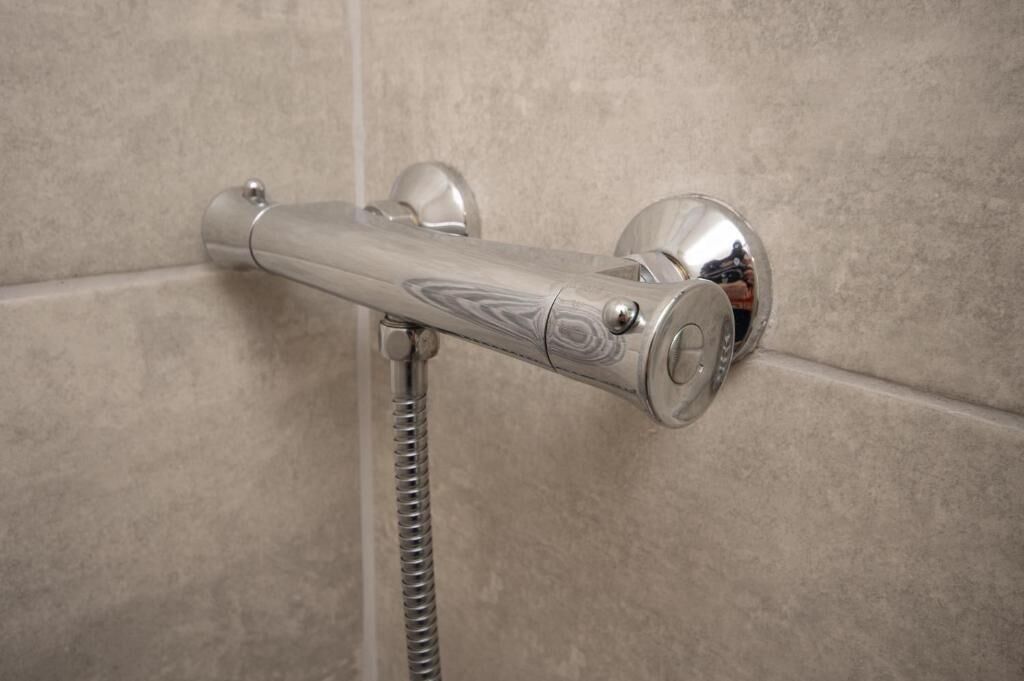 A shower with a chrome faucet and hose, mounted on a tiled wall.