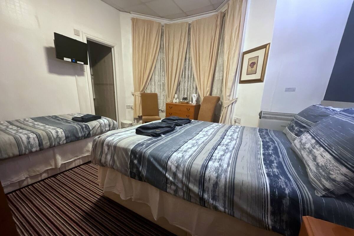 A hotel room with two beds, a flat-screen TV, a dresser, and a window with curtains.