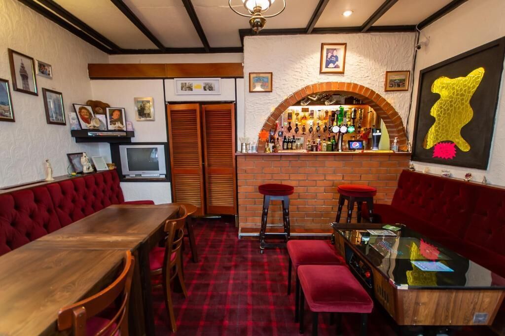 A bar area with a brick arch, red upholstered seating, and a bar counter with various bottles.