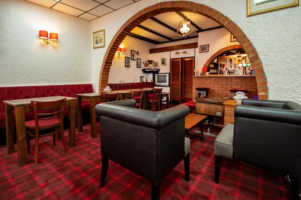 A restaurant interior with a red and white checkered floor, wooden tables and chairs, a brick archway, and a bar area.