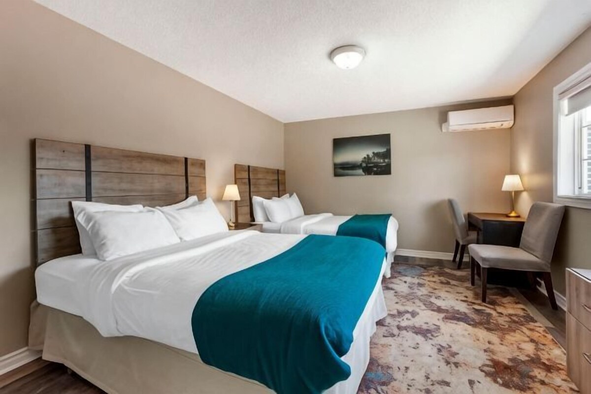 A hotel room with two beds, a desk, a chair, and a window.