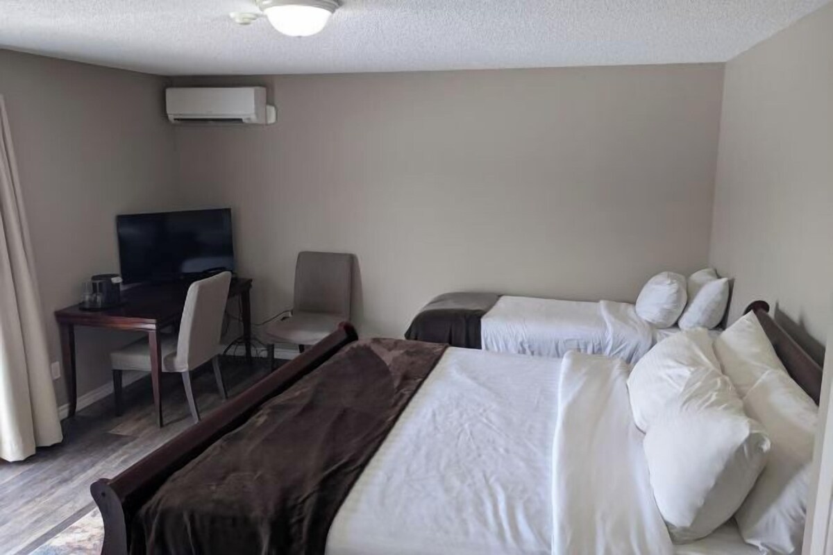A hotel room with a bed, a desk with a chair, a television, and an air conditioning unit.