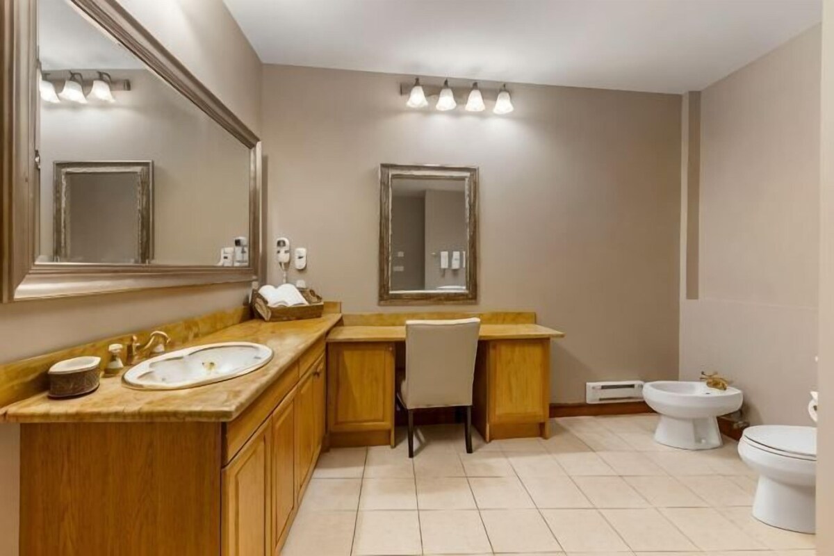 A bathroom with a sink, mirror, vanity, chair, and toilet.