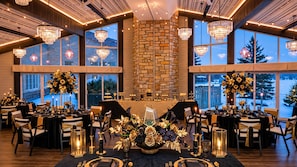 A banquet hall with multiple tables set for a formal event, featuring chandeliers, floral centerpieces, and a stone fireplace. - Christies Mill Inn & Spa, an Ascend Collection Hotel (Georgian Bay)