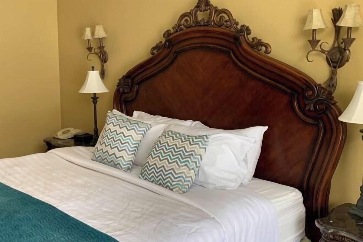 A bed with a wooden headboard, white bedding, and two patterned pillows.