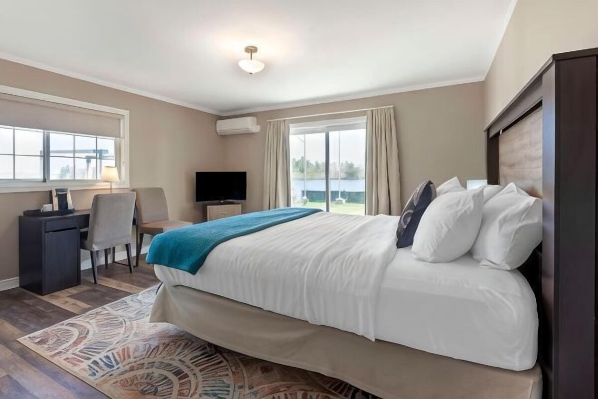 A hotel room with a large bed, a desk, a chair, a TV, and a view of the outdoors.