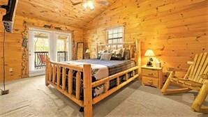 Ein Schlafzimmer in einer Blockhütte mit einem Holzbett, einem Schaukelstuhl, einem Nachttisch und einem Deckenventilator.