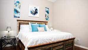 Un dormitorio con cama de madera, ropa de cama blanca y tres cuadros abstractos en la pared.