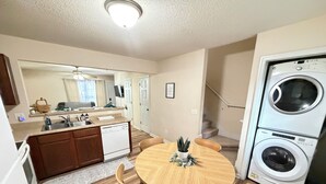 Cocina compacta con lavavajillas, comedor con mesa redonda y sillas, y lavadora y secadora integradas.