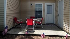 Un patio techado con una mesa y cuatro sillas, dos puertas y banderas estadounidenses en el suelo.