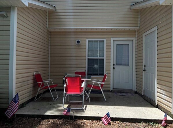 Un patio couvert avec une table et quatre chaises, deux portes et des drapeaux américains disposés sur le sol.