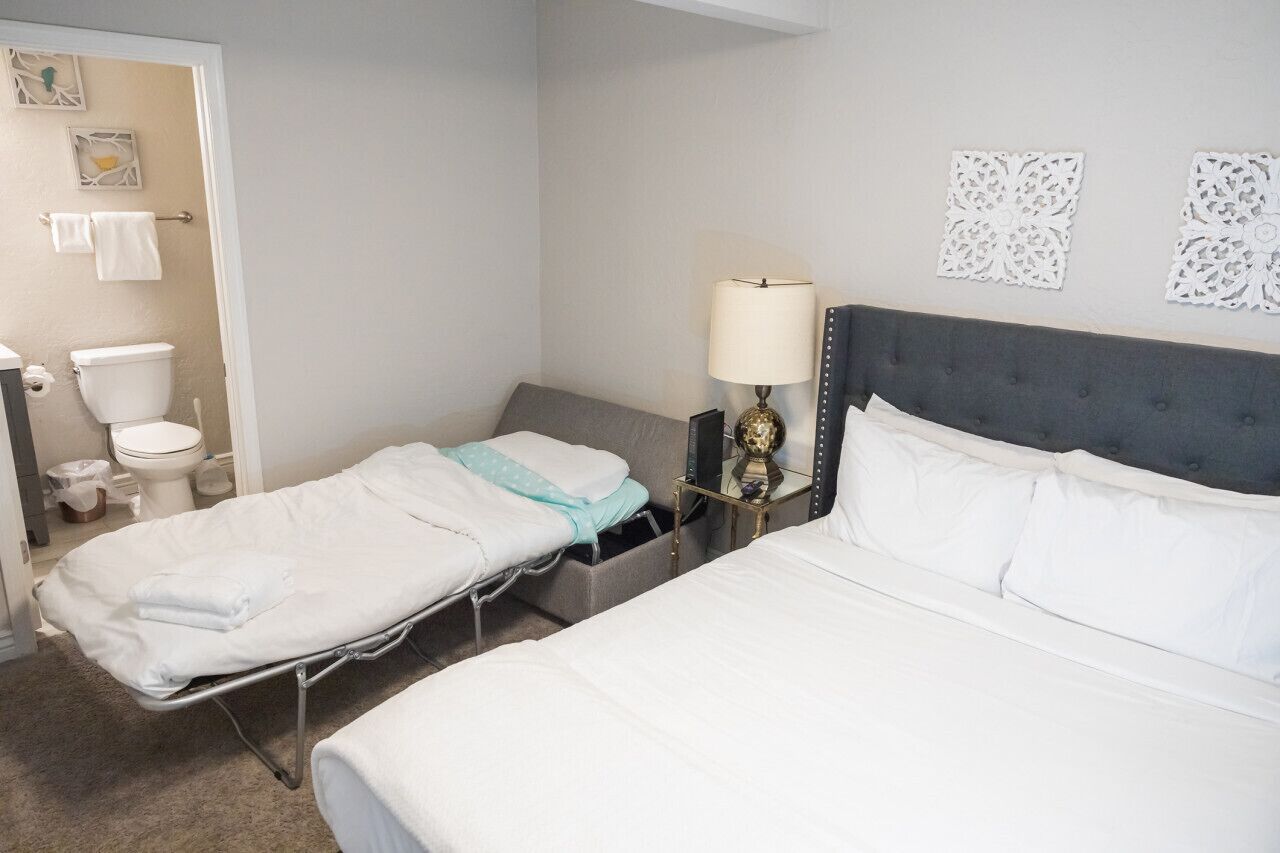 A hotel room with a bed, bedside table, lamp, and a small bedside cabinet.