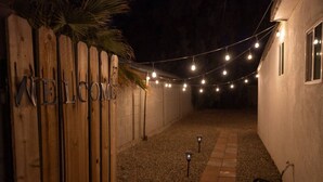 Un cortile con recinto in legno, un cartello di benvenuto, luci a catena e un vialetto in ghiaia.