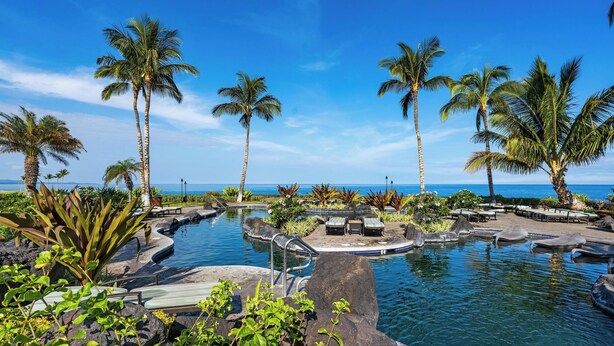 A pool area with palm trees, lounge chairs, and a view of the ocean.