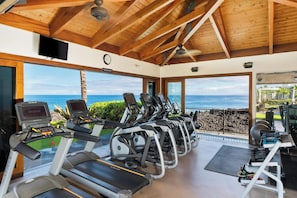 A gym with treadmills and elliptical machines, large windows with a view of the ocean, and a wooden ceiling. - Ocean Front with stunning views! Includes beach gear! Halii Kai 15H (Waikoloa Beach Resort)