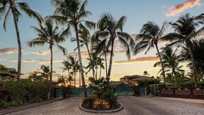 A paved entrance with a sign reading "Hawai Kai" surrounded by palm trees and a sunset in the background.