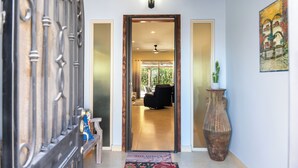 A hallway with a wooden door leading to a room with a ceiling fan, a large vase, and a painting on the wall.
