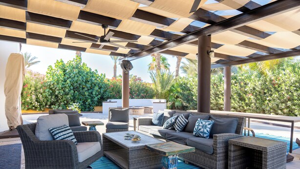 An outdoor patio with wicker furniture, a blue striped rug, and a ceiling with a geometric pattern.