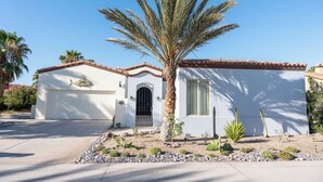 A single-story house with a white exterior, a tiled roof, and a palm tree in the front yard.