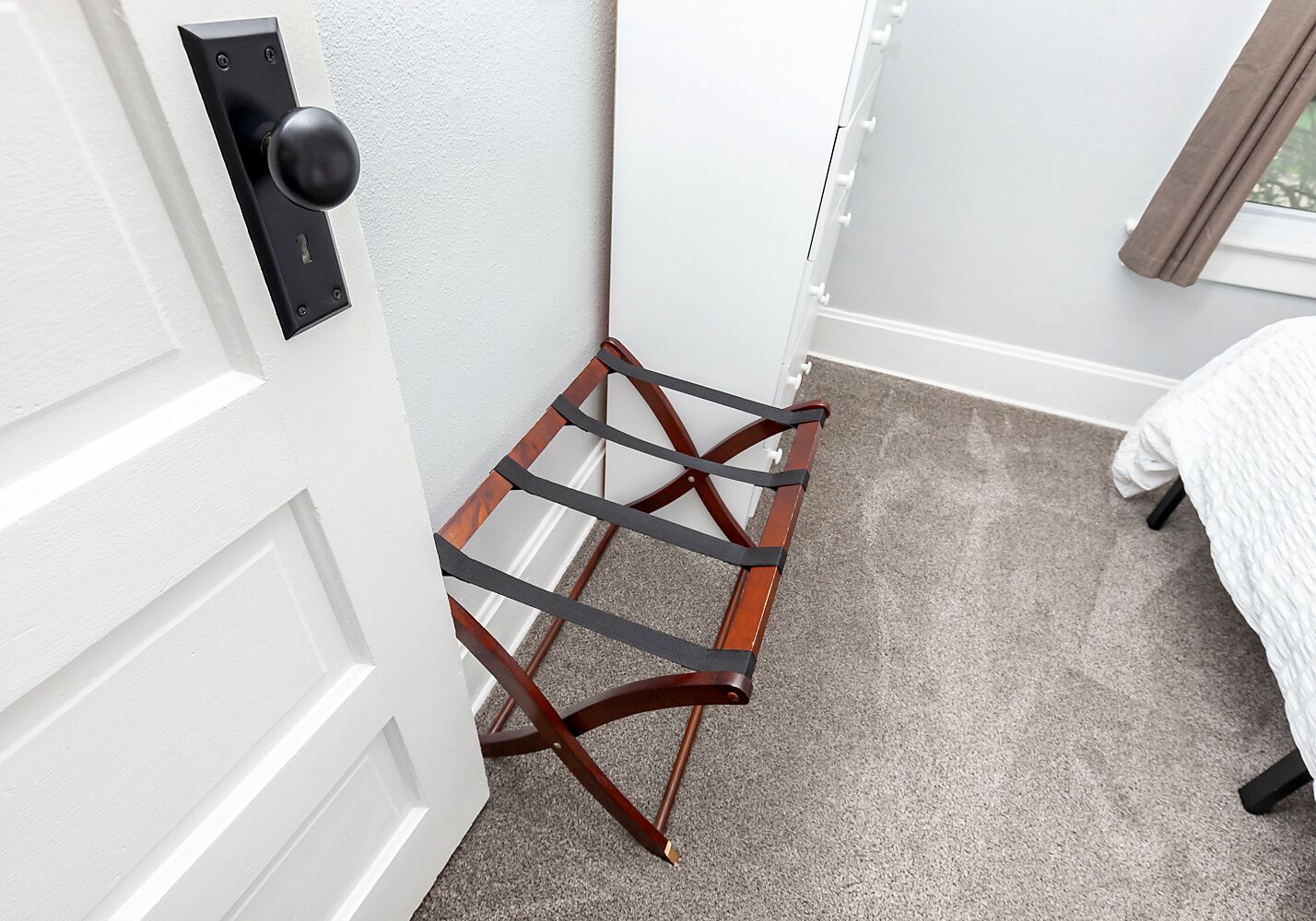 Een kamer met een witte deur, een houten stoel met metalen frame en een beige tapijt.