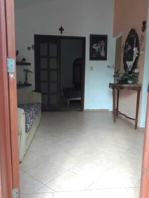 A room with a tiled floor, a sofa with a patterned cover, a wooden table with a mirror, and a door with a cross above it.