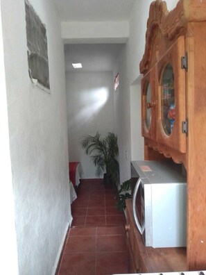 A narrow hallway with a tiled floor, a wooden cabinet with glass doors, and a white wall with a small window.