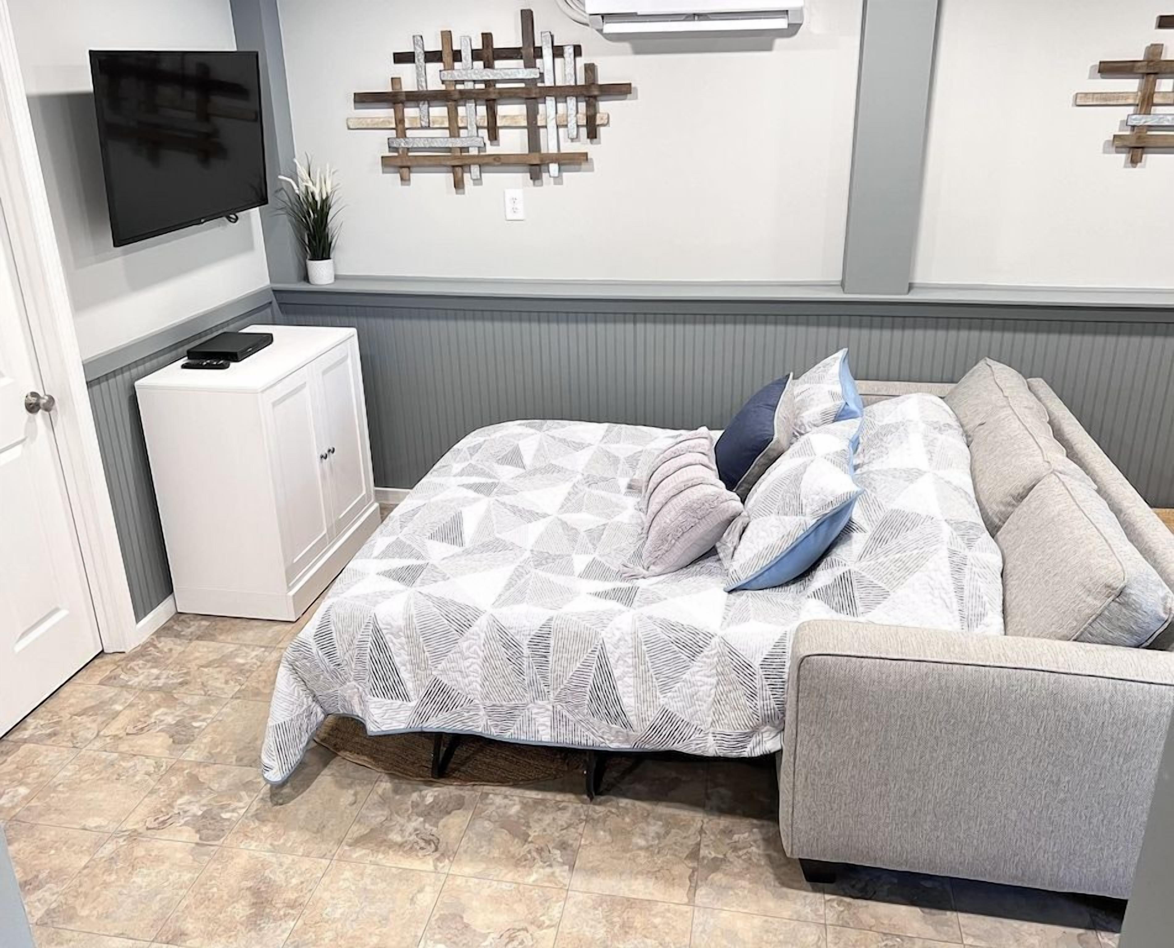 Un dormitorio con cama, televisor, un armario blanco y una lámpara fijada a la pared.