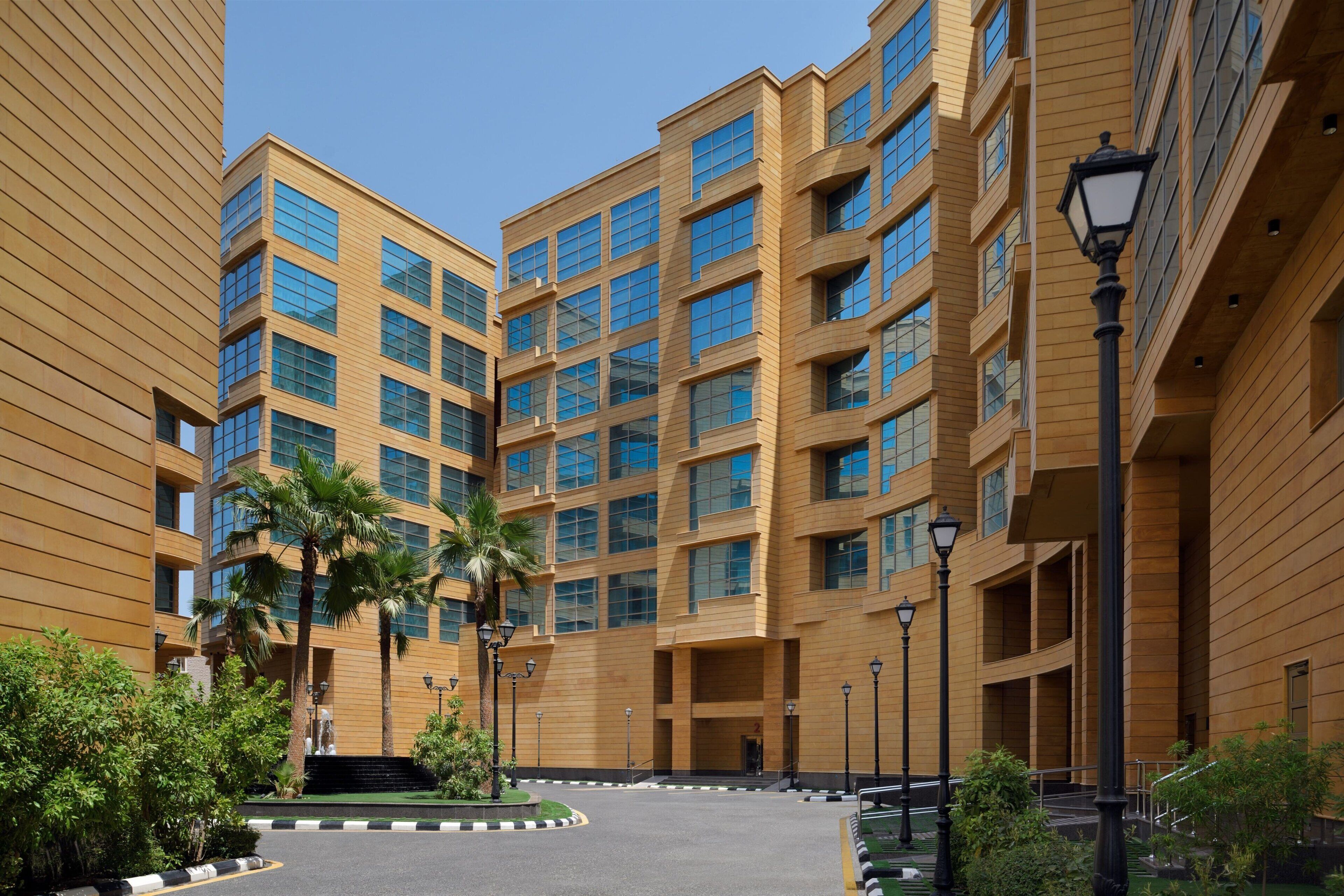 A modern multi-story building with a symmetrical facade, large windows, and a central courtyard with palm trees and a fountain.