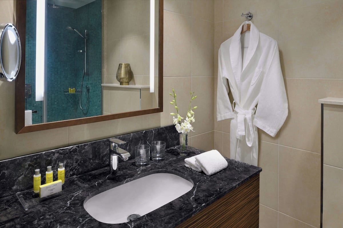 A bathroom with a marble sink, a mirror, a robe hanging, and a vase with flowers.