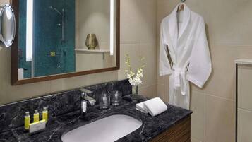 A bathroom with a marble sink, a mirror, a robe hanging, and a vase with flowers.