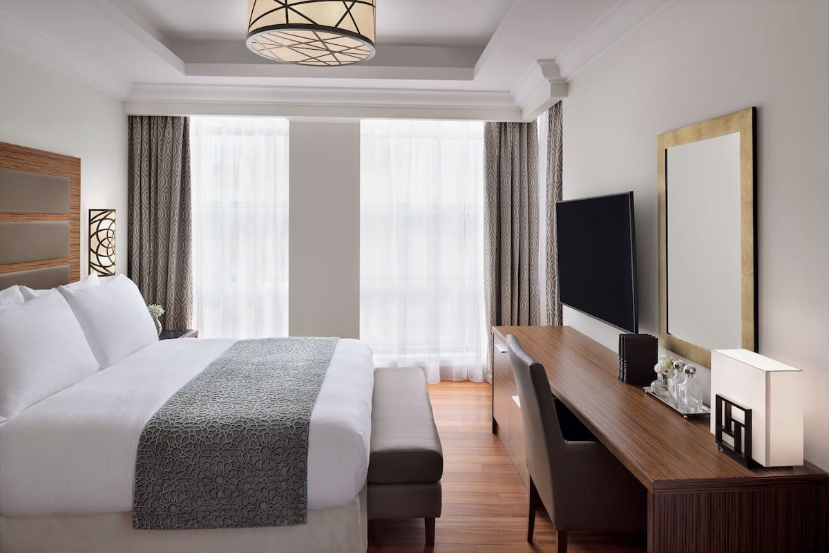 A hotel room with a large bed, a desk with a chair, a television, and a large mirror.